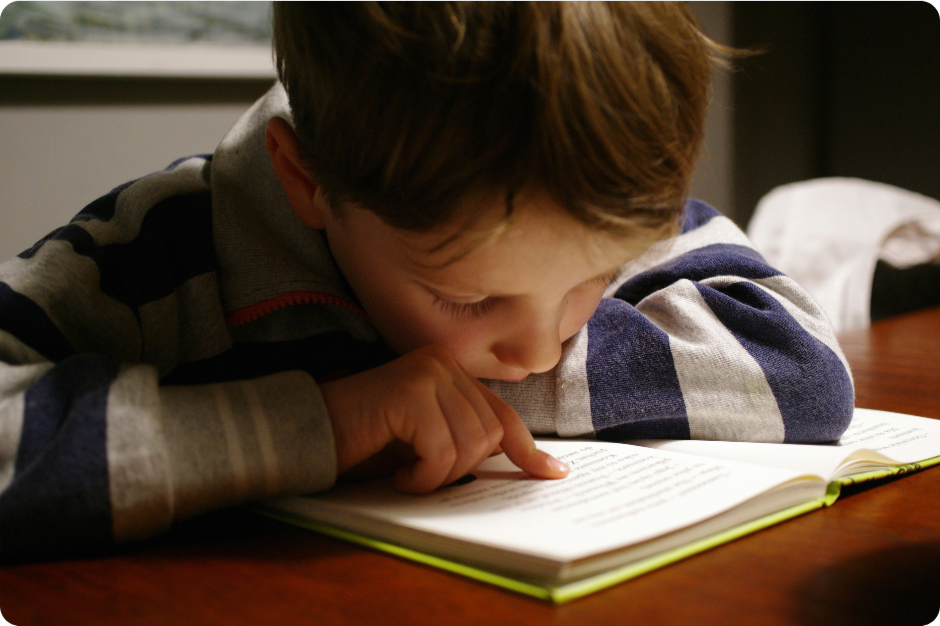 A child, possibly with ADHD, focusing intently on reading, up close and guided by a finger.