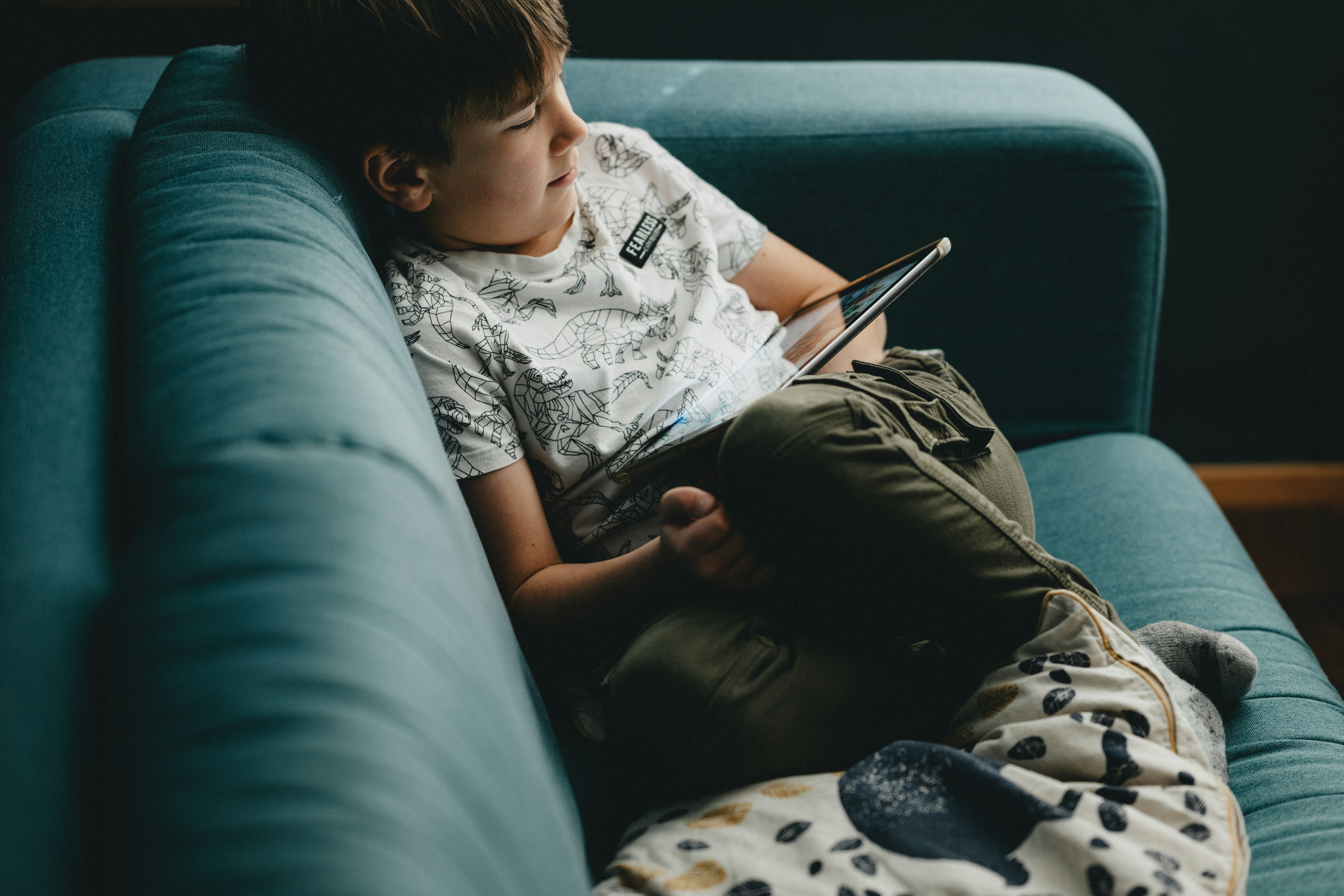 Eight year old boy sitting on a blue couch with an ipad in his lap.