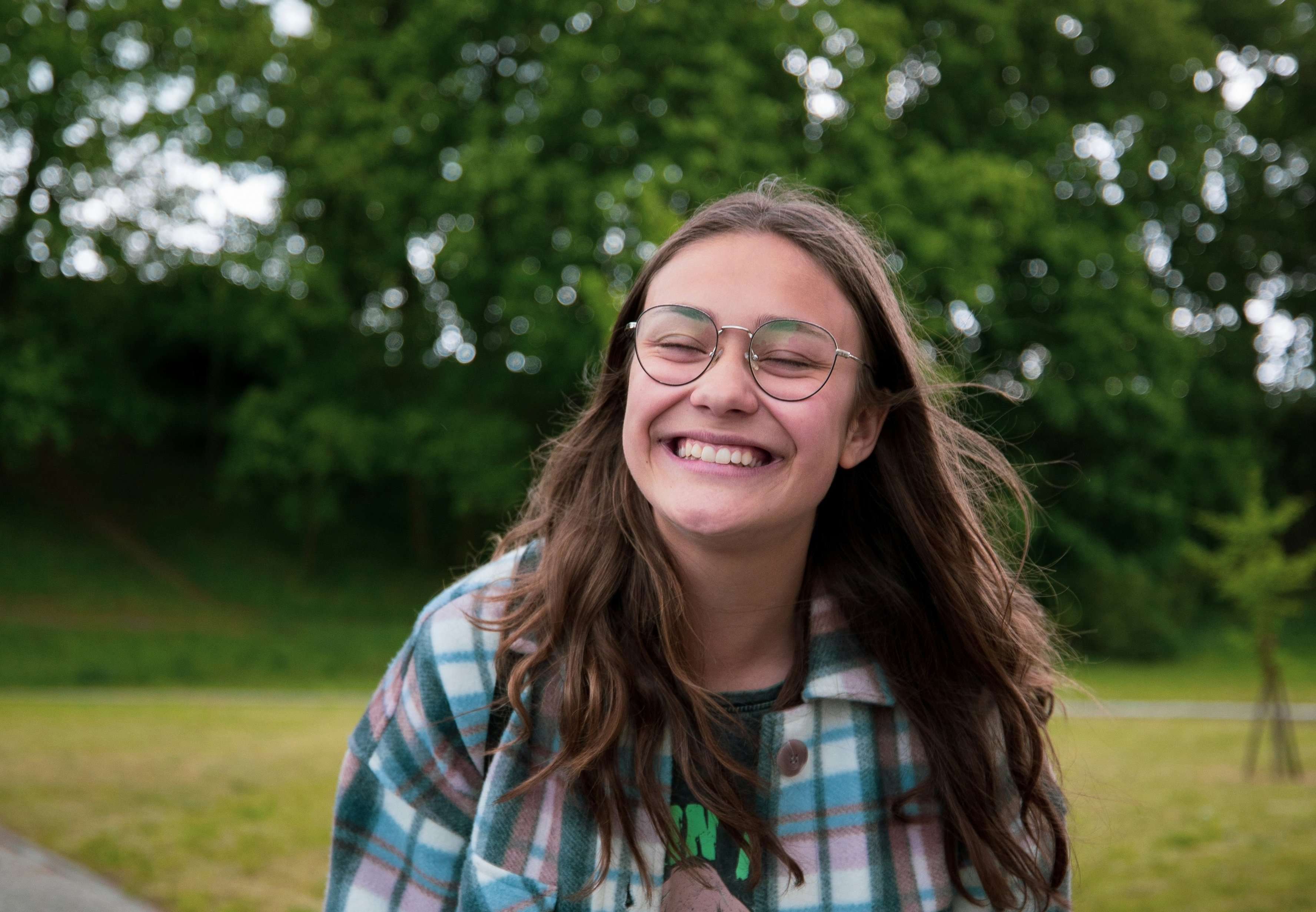 An image of a teenage girl with long brown hair wearing glasses and a plaid flannel shirt with a big smile.
